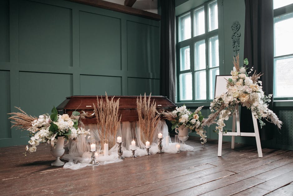 A floral arrangement featuring white roses, ivory orchids, and soft pink blooms, complemented by tall, beige pampas grass and eucalyptus leaves, arranged in white ceramic vases placed on a rustic wood